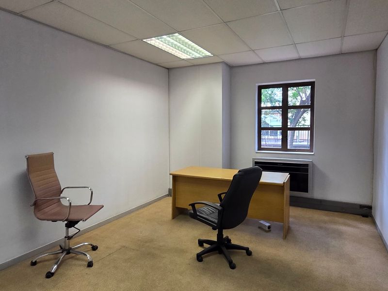A functional office space featuring a suspended ceiling, recessed lighting, carpeted flooring, and a window with an integrated HVAC unit.