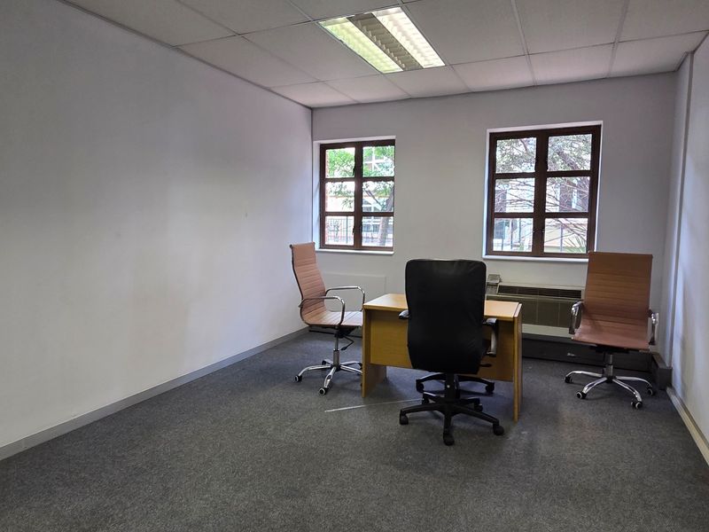 A functional office space featuring carpeted flooring, a suspended ceiling with recessed lighting, and an integrated HVAC unit under the windows.