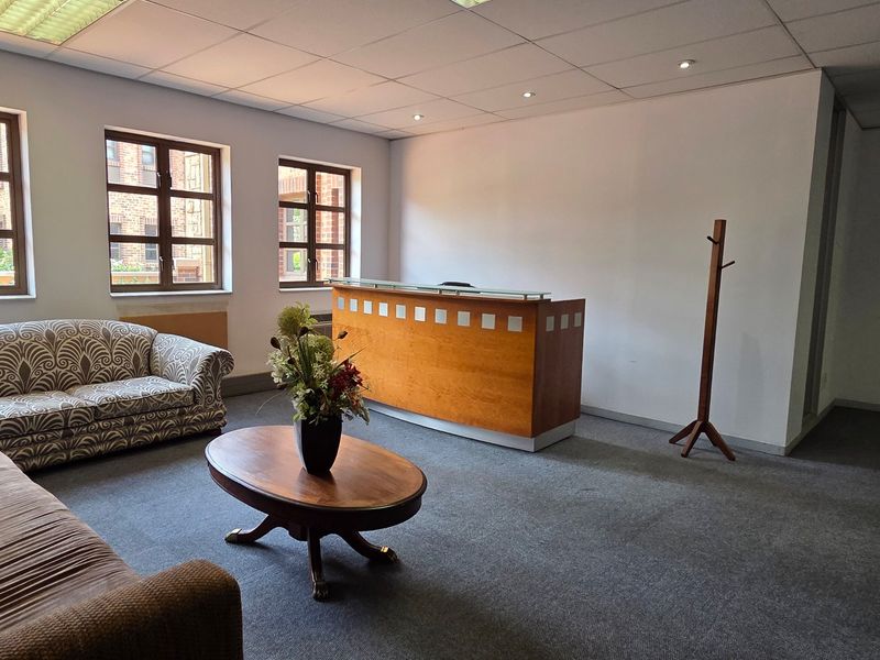 A professional office reception area featuring a built-in wooden desk, carpeted flooring, and a suspended ceiling with recessed lighting.