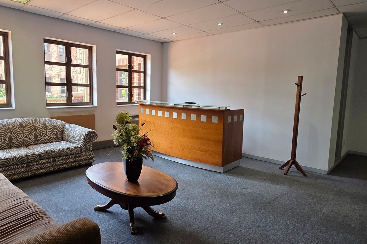A professional office reception area featuring a built-in wooden desk, carpeted flooring, and a suspended ceiling with recessed lighting.