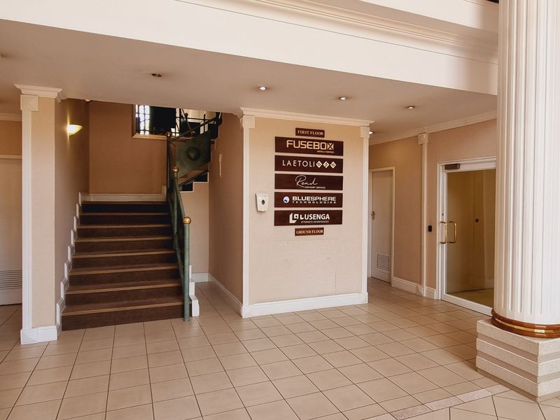 Spacious office building entrance lobby featuring tiled flooring, a central directory board, and a staircase leading to the first floor.
