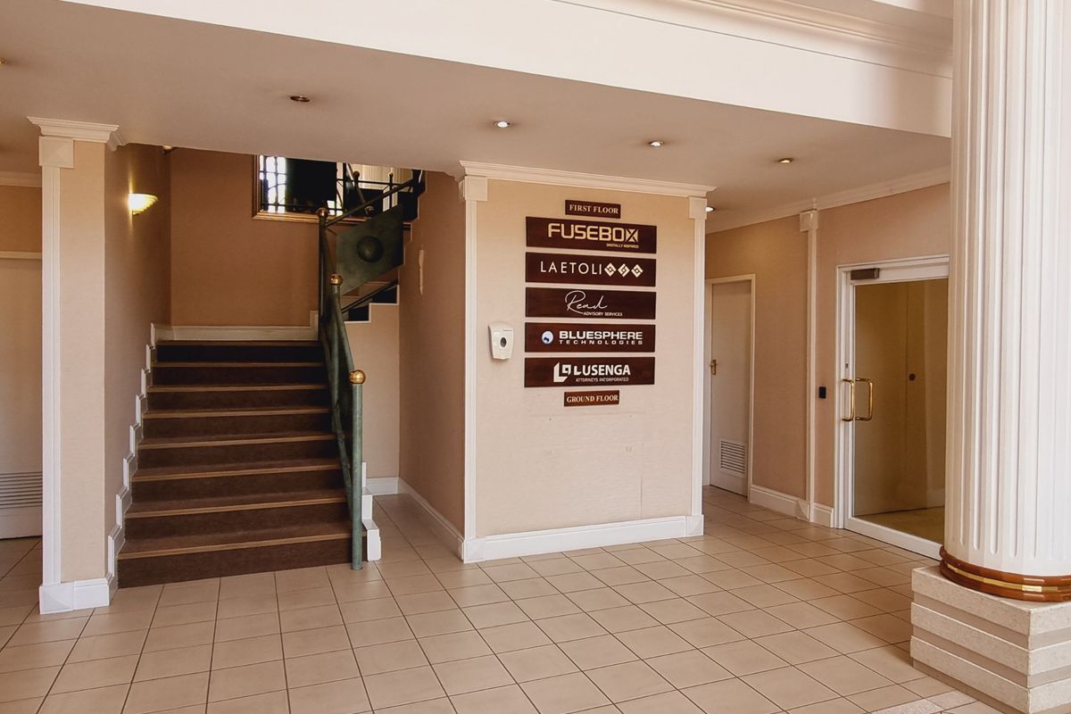 Spacious office building entrance lobby featuring tiled flooring, a central directory board, and a staircase leading to the first floor.