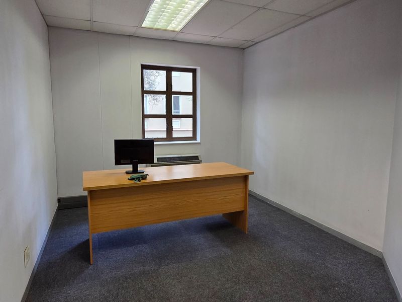 A functional office space featuring a suspended ceiling, recessed lighting, and a window with an integrated HVAC unit.