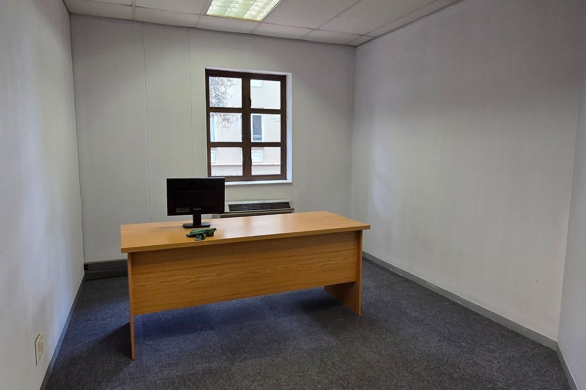 A functional office space featuring a suspended ceiling, recessed lighting, and a window with an integrated HVAC unit.
