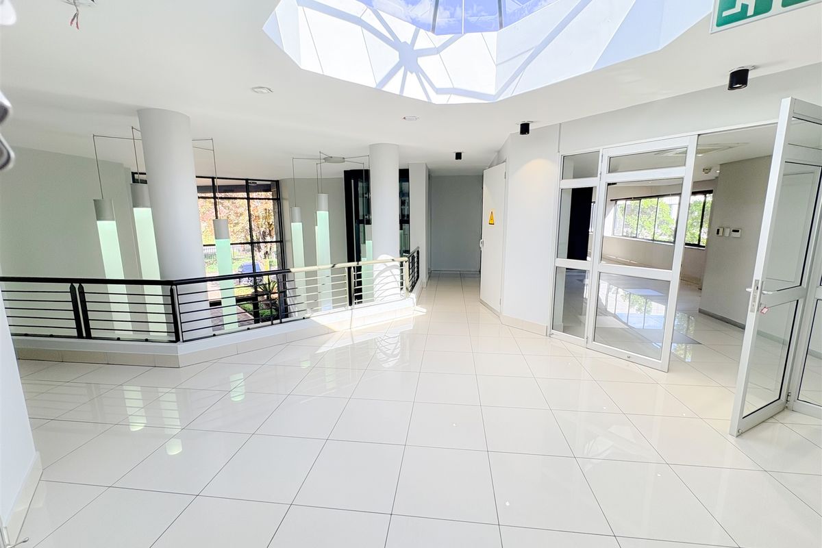 Bright and spacious office lobby featuring polished tile flooring, a large central skylight, and modern glass partition doors.