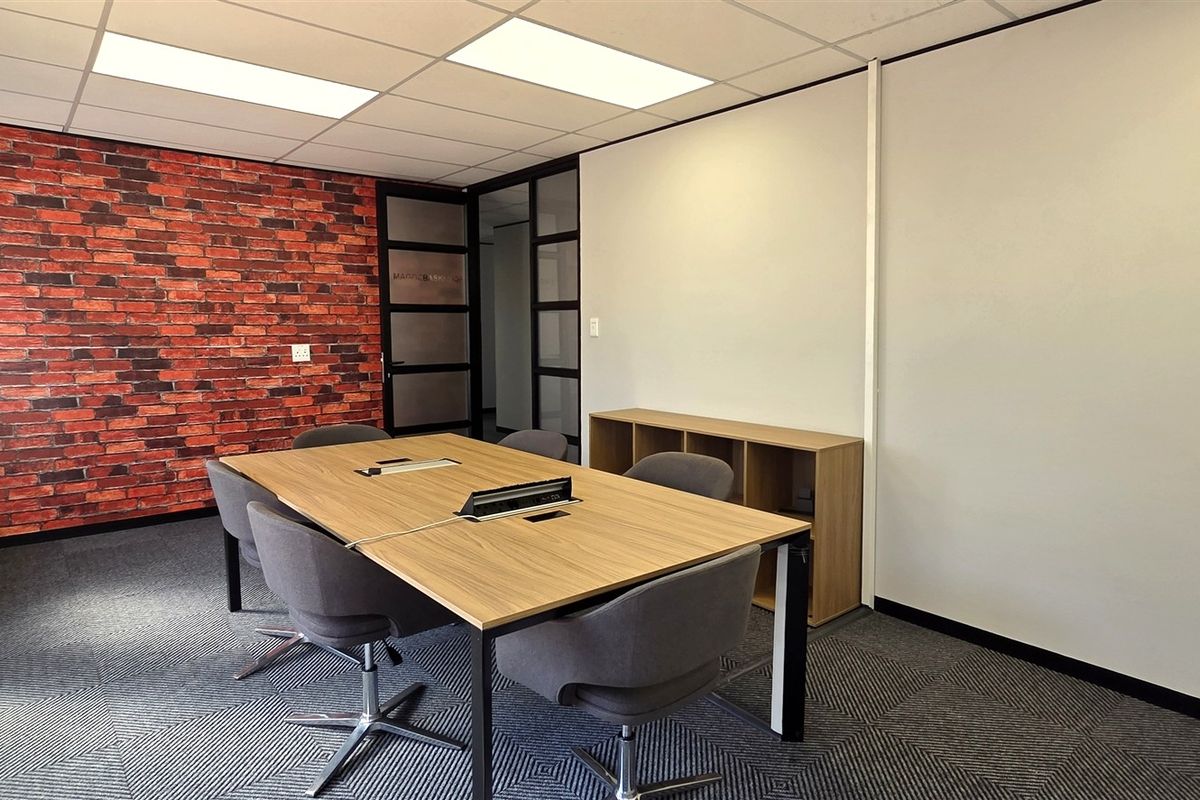A modern office meeting room featuring a brick accent wall, suspended ceiling with recessed lighting, and professional carpet tile flooring.