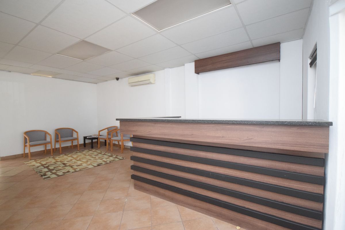A professional office reception area featuring a built-in wooden reception desk, tiled flooring, and a suspended ceiling with integrated air conditioning.