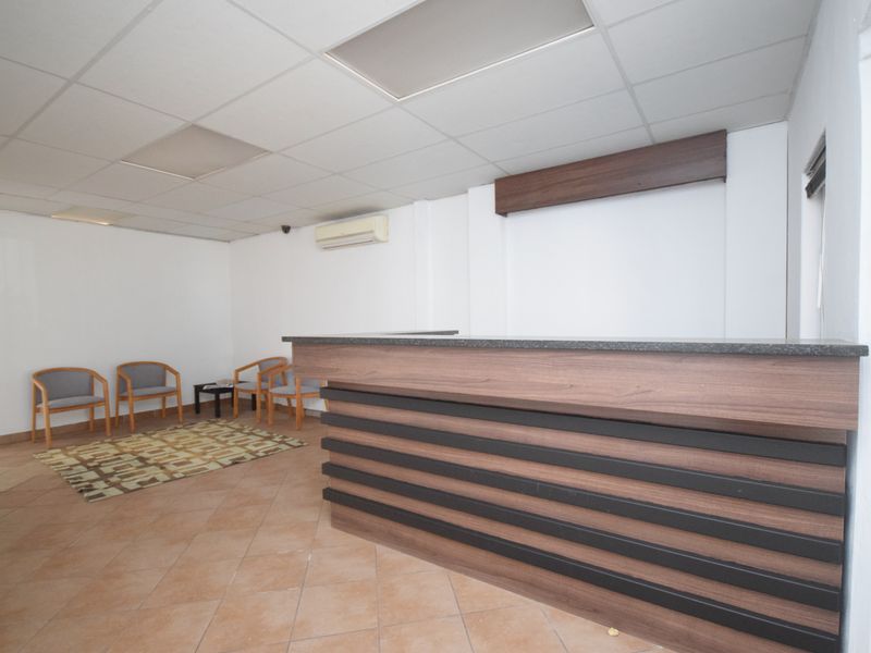 A professional office reception area featuring a built-in wooden reception desk, tiled flooring, and a suspended ceiling with integrated air conditioning.