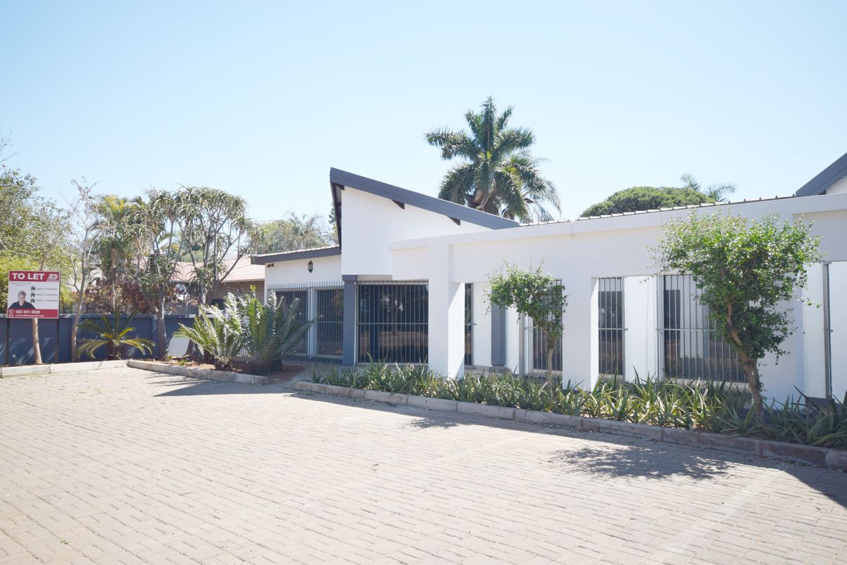 Front exterior view of the office property featuring a paved driveway, white facade, and secure window bars.