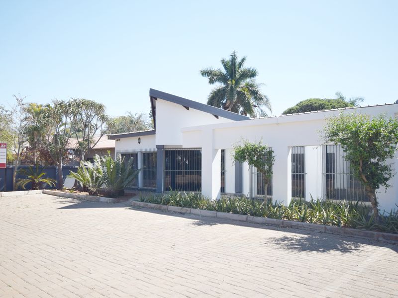 Front exterior view of the office property featuring a paved driveway, white facade, and secure window bars.