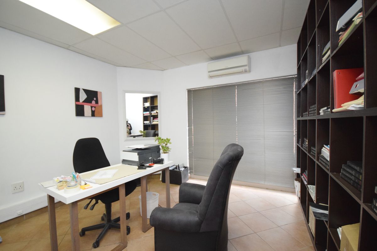 A functional office space featuring tiled flooring, a suspended ceiling, an integrated air conditioning unit, and extensive built-in shelving.