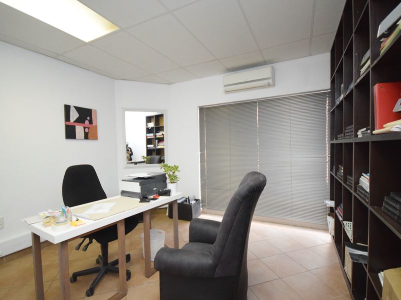 A functional office space featuring tiled flooring, a suspended ceiling, an integrated air conditioning unit, and extensive built-in shelving.