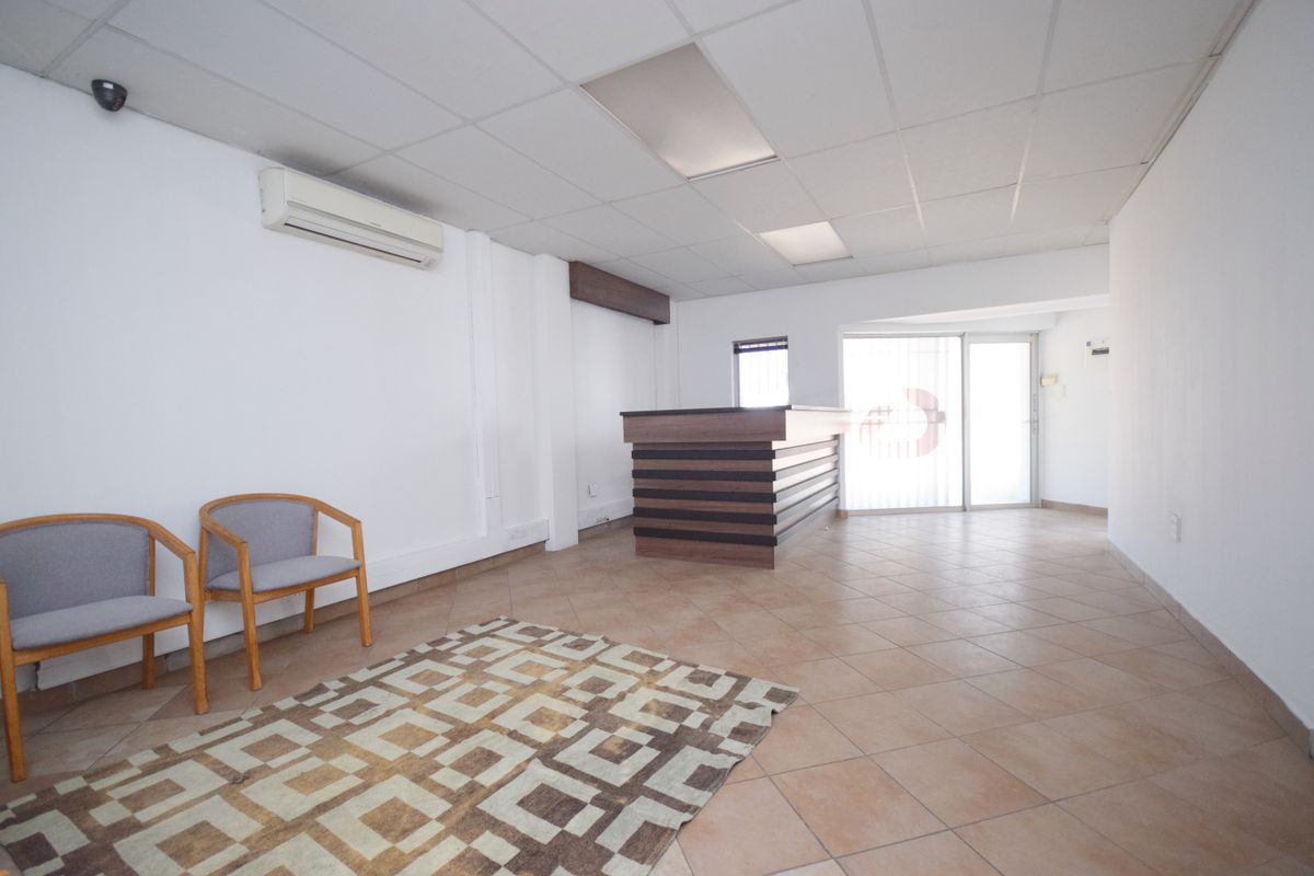 A professional office reception area featuring ceramic tile flooring, a built-in reception desk, suspended ceiling, and wall-mounted air conditioning unit.