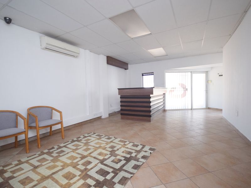 A professional office reception area featuring ceramic tile flooring, a built-in reception desk, suspended ceiling, and wall-mounted air conditioning unit.