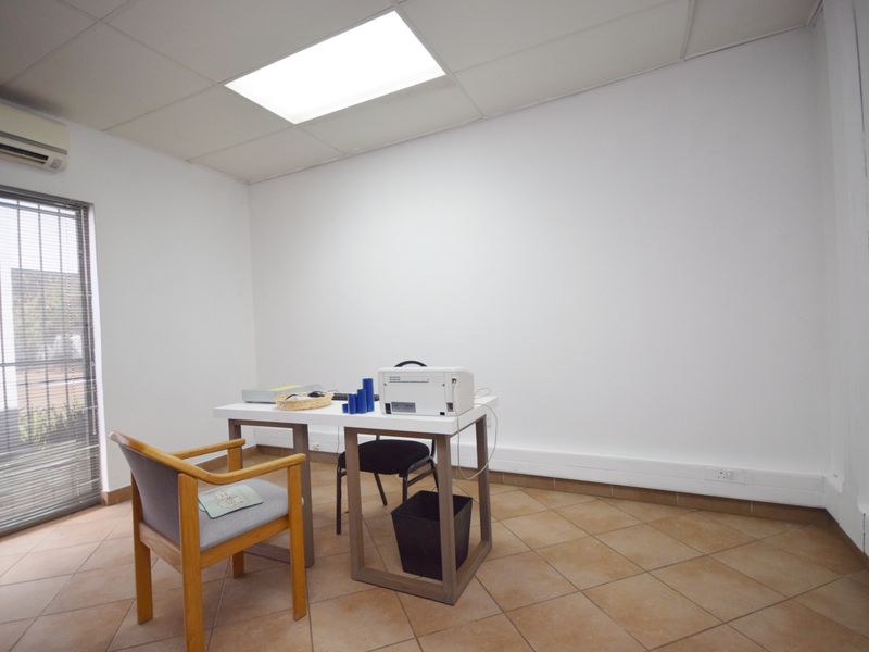 A functional office space featuring tiled flooring, a drop ceiling with recessed lighting, and an integrated air conditioning unit.