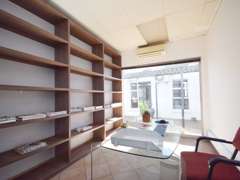 A functional office space featuring extensive built-in wooden shelving, tiled flooring, and a split-system air conditioner with direct access to an outdoor area.