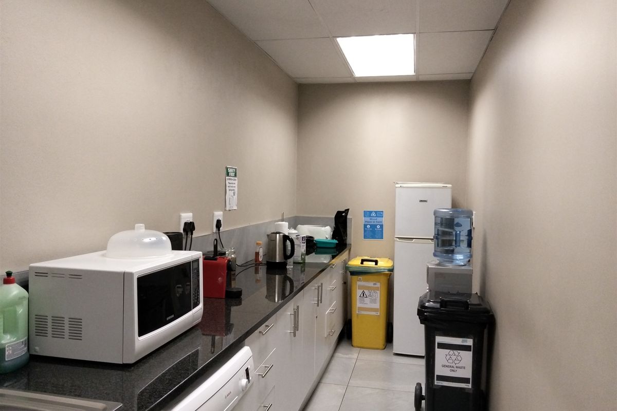 A functional industrial kitchen area featuring granite countertops, ample built-in cabinetry, a stainless steel sink, and durable tiled flooring.