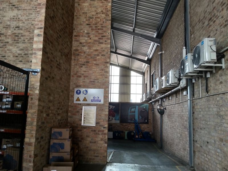 Spacious industrial utility area featuring exposed brick walls, high-pitched corrugated metal roofing, and multiple wall-mounted air conditioning units.