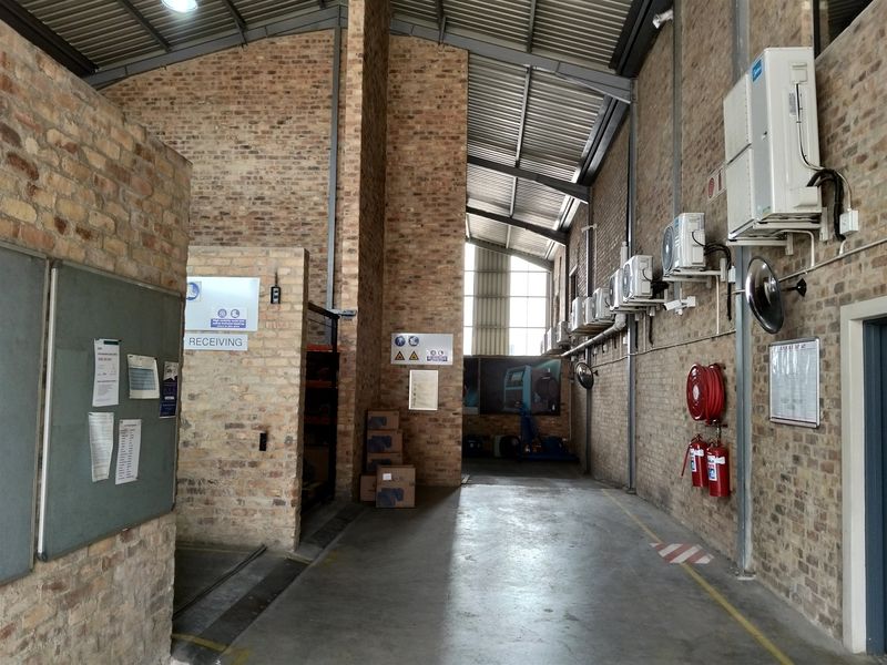 Spacious industrial utility area featuring exposed brick walls, high steel truss ceilings, concrete flooring, and wall-mounted air conditioning units with integrated fire safety equipment.