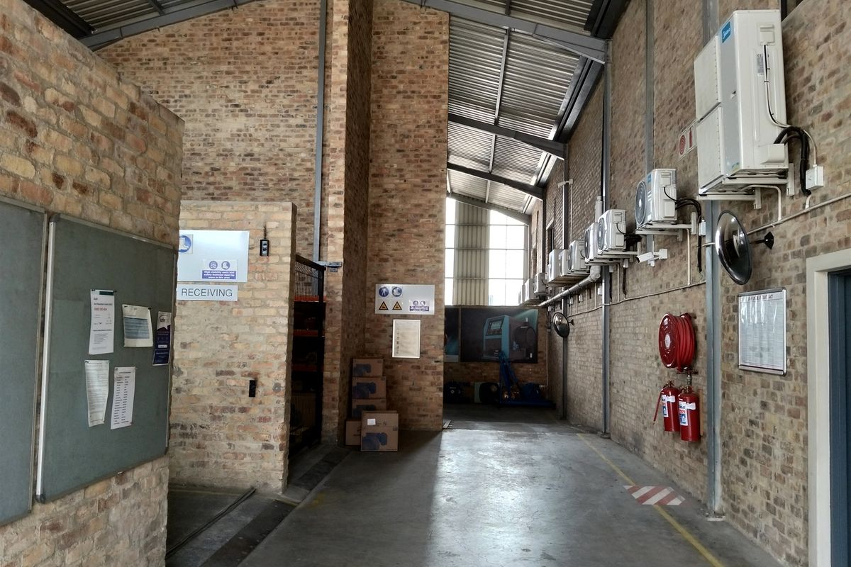 Spacious industrial utility area featuring exposed brick walls, high steel truss ceilings, concrete flooring, and wall-mounted air conditioning units with integrated fire safety equipment.