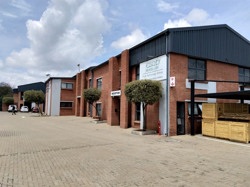 Front exterior view of a well-maintained industrial building featuring brick facade, metal roofing, and a paved driveway with a designated reception entrance.
