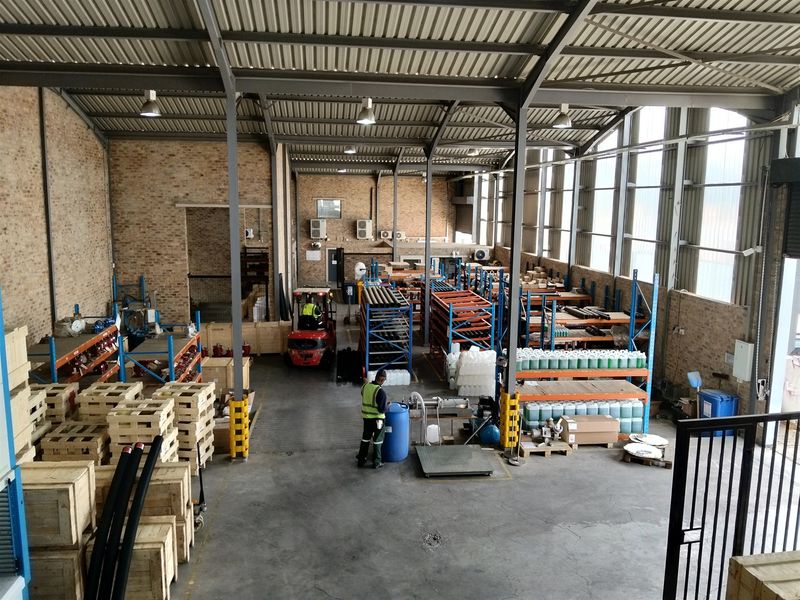 Spacious industrial warehouse featuring exposed brick walls, high steel truss ceilings, concrete flooring, and large windows providing ample natural light for operations.