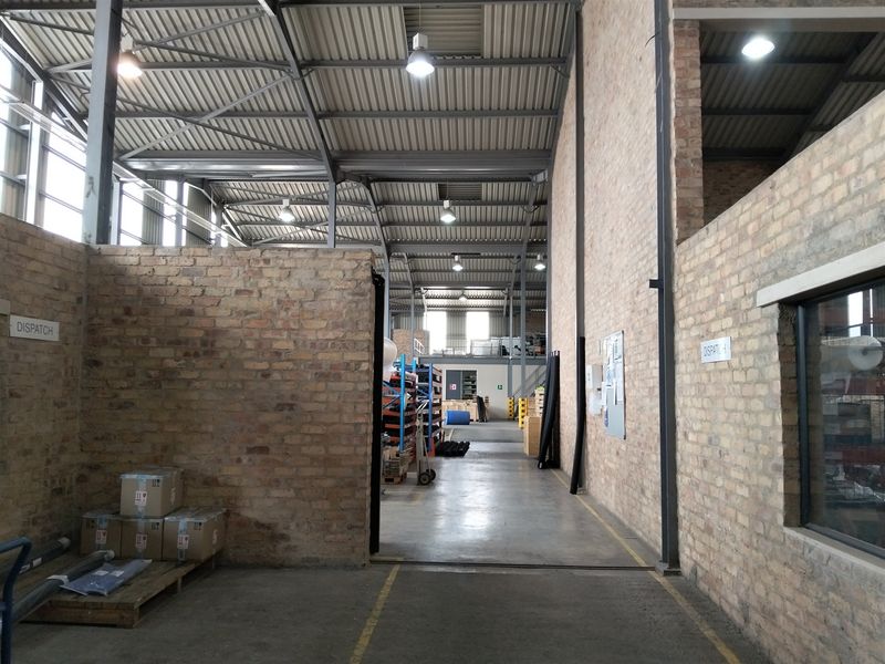 Spacious industrial warehouse interior featuring exposed brick walls, high steel truss ceilings, and durable concrete flooring, suitable for logistics or manufacturing operations.