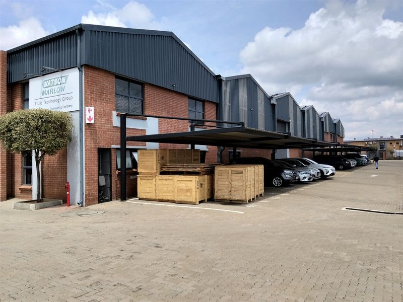 Industrial facility featuring a brick facade, corrugated metal roofing, and covered parking bays with a paved driveway.