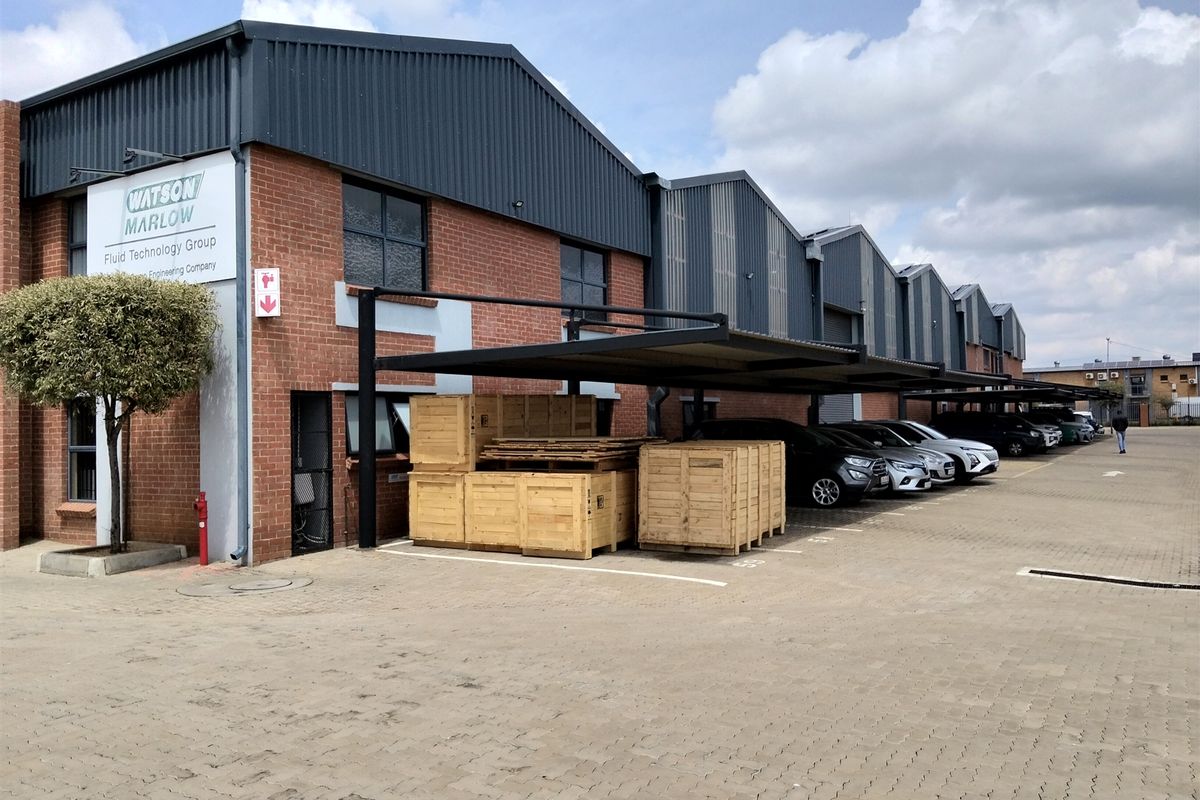 Industrial facility featuring a brick facade, corrugated metal roofing, and covered parking bays with a paved driveway.