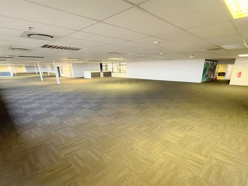 A spacious, open-plan office area featuring carpeted flooring, a suspended ceiling with recessed lighting, and integrated air conditioning infrastructure.