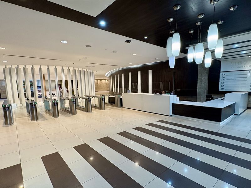 Modern office building lobby featuring a professional reception desk, secure turnstile access control, and contemporary lighting fixtures with polished tiled flooring.