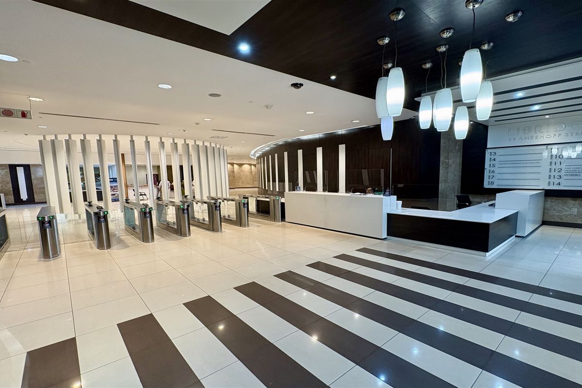 Modern office building lobby featuring a professional reception desk, secure turnstile access control, and contemporary lighting fixtures with polished tiled flooring.