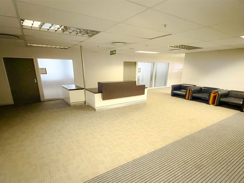 A professional office reception area featuring a built-in reception desk, suspended ceiling with recessed lighting, and neutral carpet flooring.