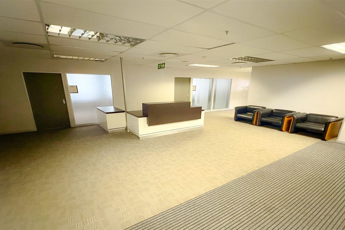A professional office reception area featuring a built-in reception desk, suspended ceiling with recessed lighting, and neutral carpet flooring.