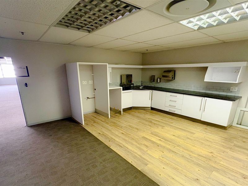 A functional office kitchenette featuring white cabinetry, a sink, and a mix of carpet and laminate flooring, suitable for staff breakroom use.