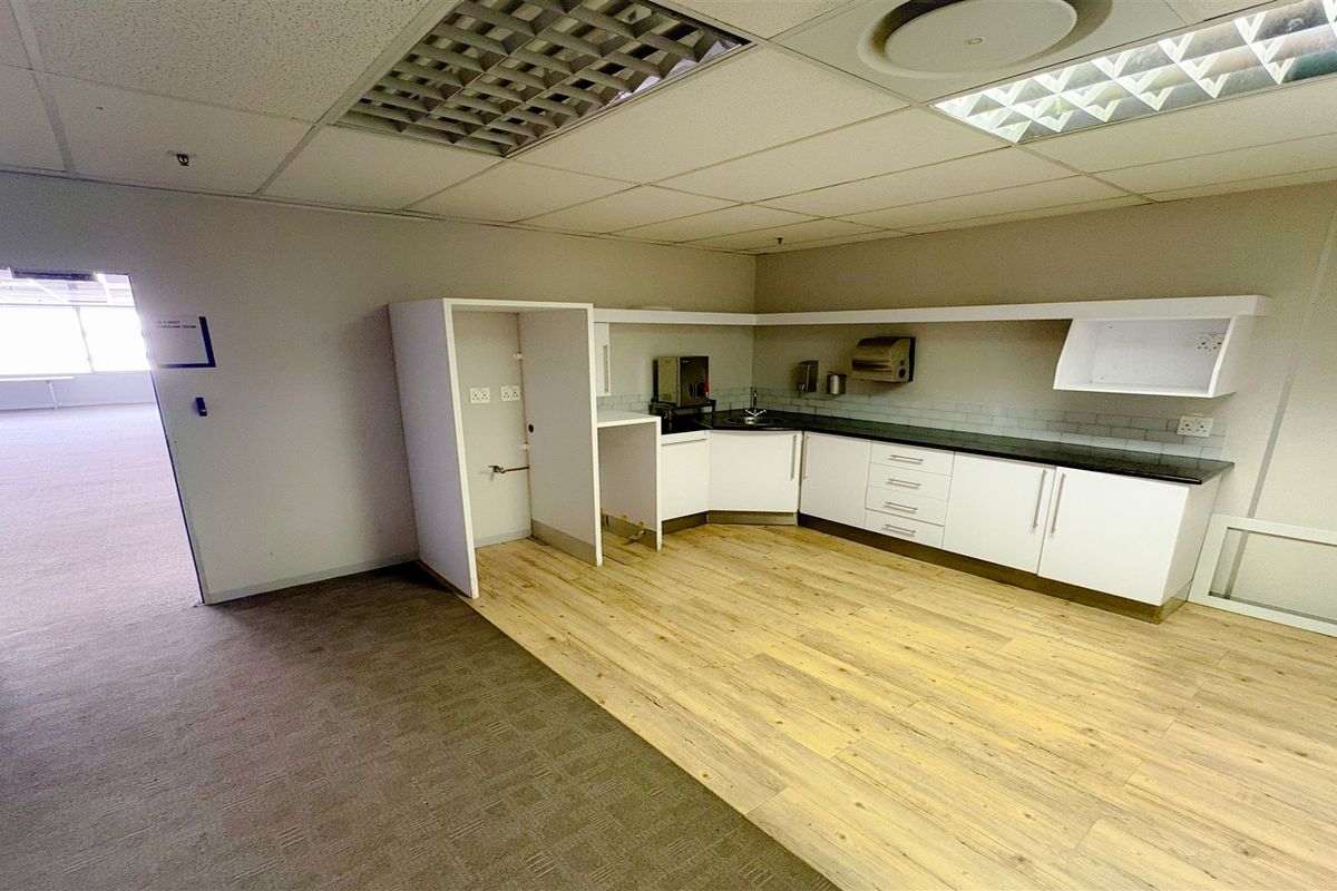 A functional office kitchenette featuring white cabinetry, a sink, and a mix of carpet and laminate flooring, suitable for staff breakroom use.