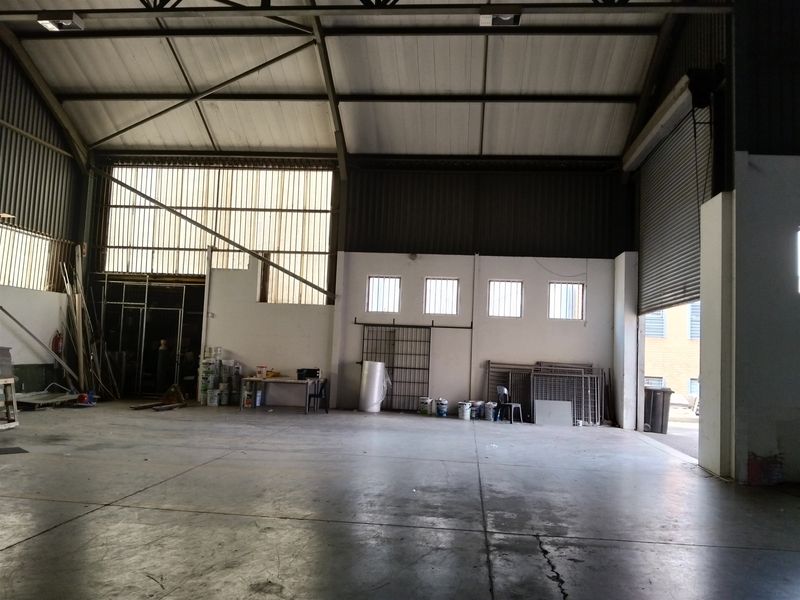 Spacious industrial warehouse unit featuring high ceilings, concrete flooring, and a large roller shutter door for easy access.