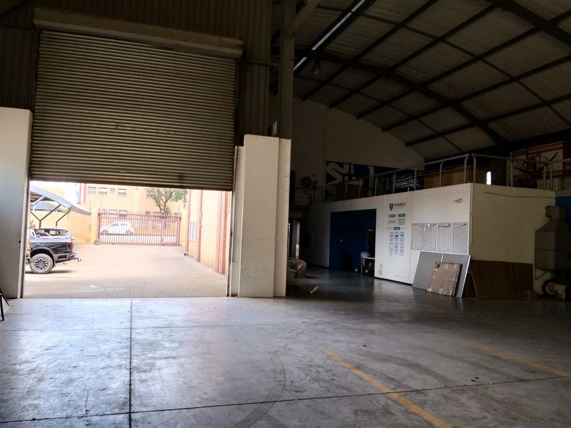Spacious industrial warehouse unit featuring a large roller shutter door, concrete flooring, and an integrated mezzanine level for additional storage or office space.