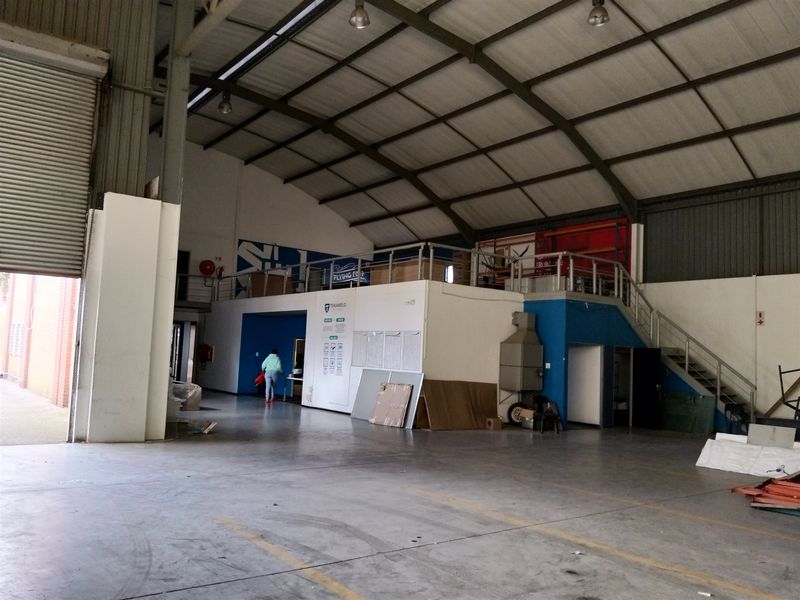 Spacious industrial warehouse featuring a high-clearance roof, concrete flooring, a functional mezzanine level with staircase access, and a large roller shutter door for loading.