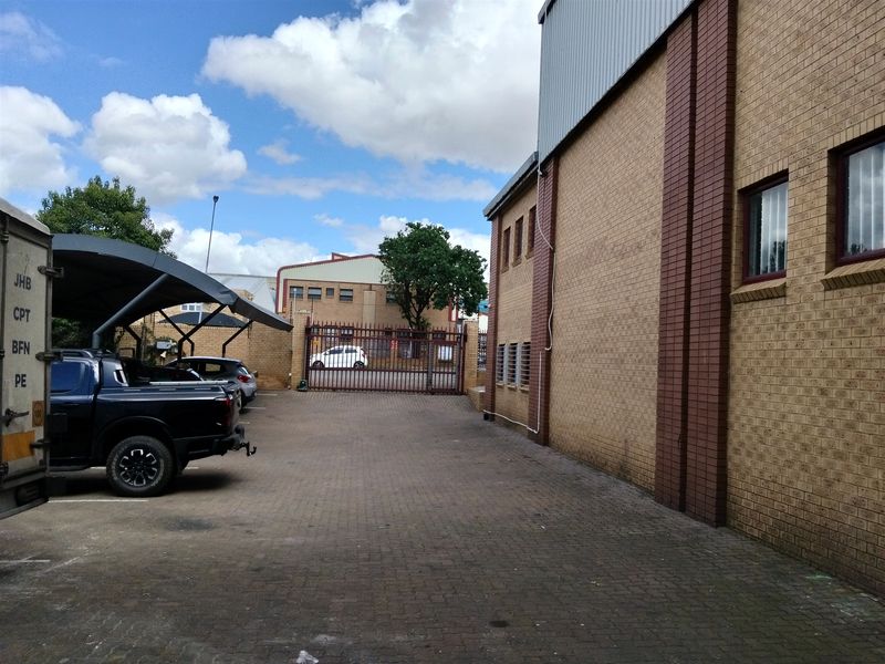Rear exterior view of the industrial property featuring a paved driveway, face brick facade, and secure gated access.