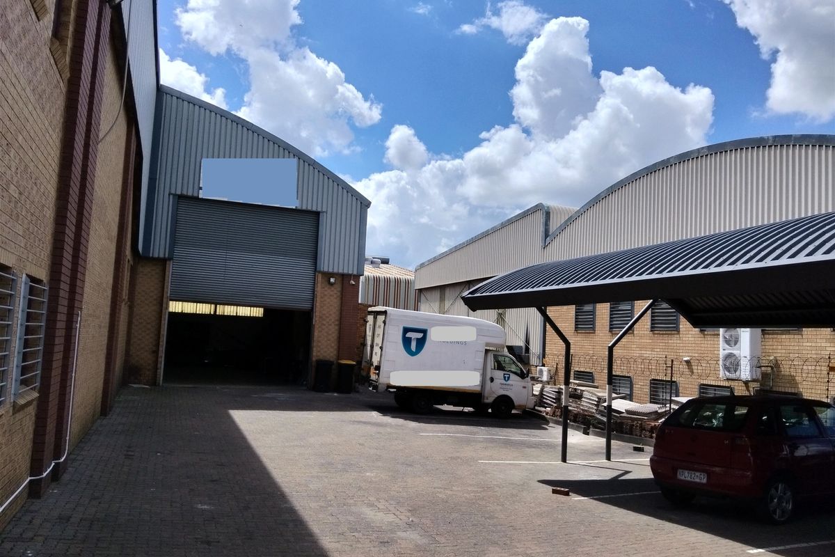 Industrial rear yard featuring a large roller shutter door, paved parking area, and a covered carport structure.
