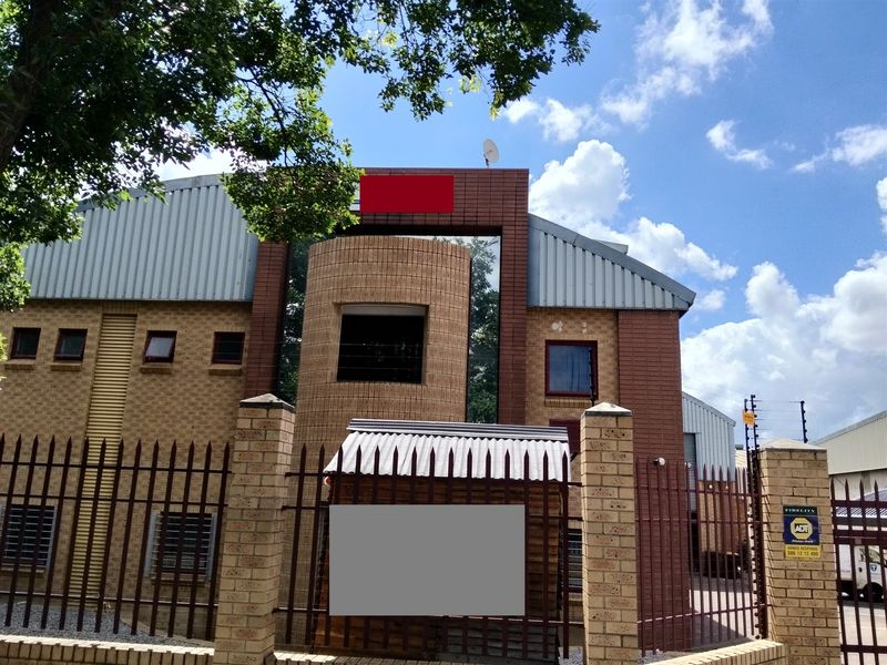 Front exterior view of an industrial property featuring a face brick facade, corrugated metal roofing, and secure perimeter fencing with integrated security systems.