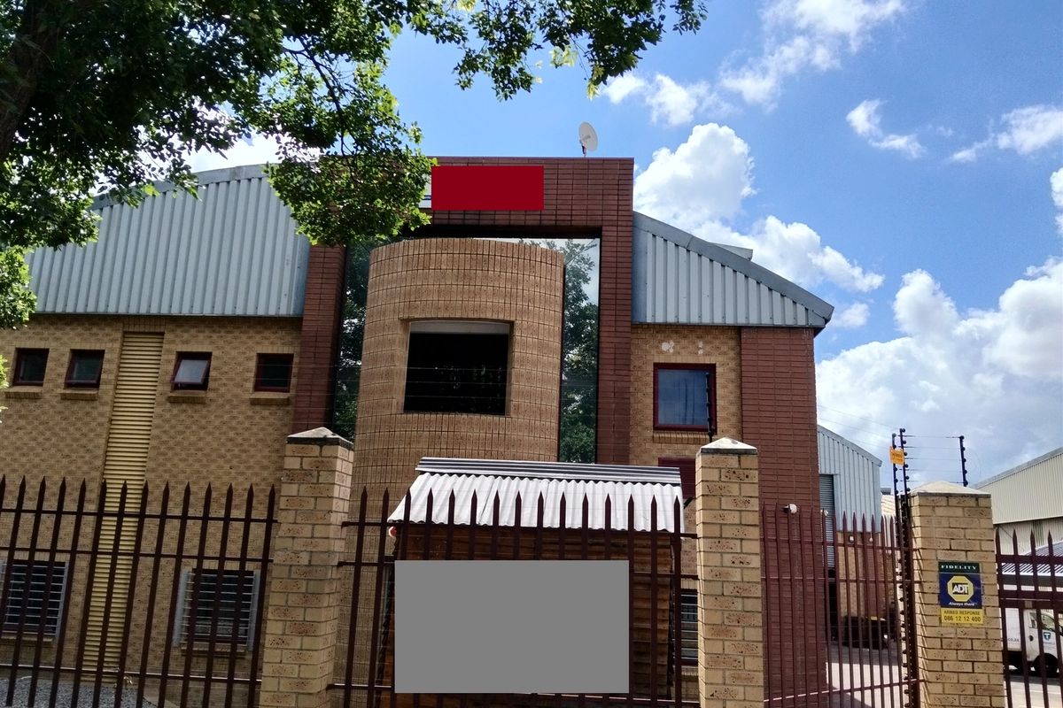Front exterior view of an industrial property featuring a face brick facade, corrugated metal roofing, and secure perimeter fencing with integrated security systems.