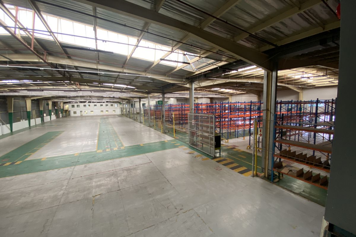 Spacious industrial warehouse featuring high ceilings with skylights, durable epoxy-coated concrete flooring, and extensive built-in steel racking systems for efficient storage.