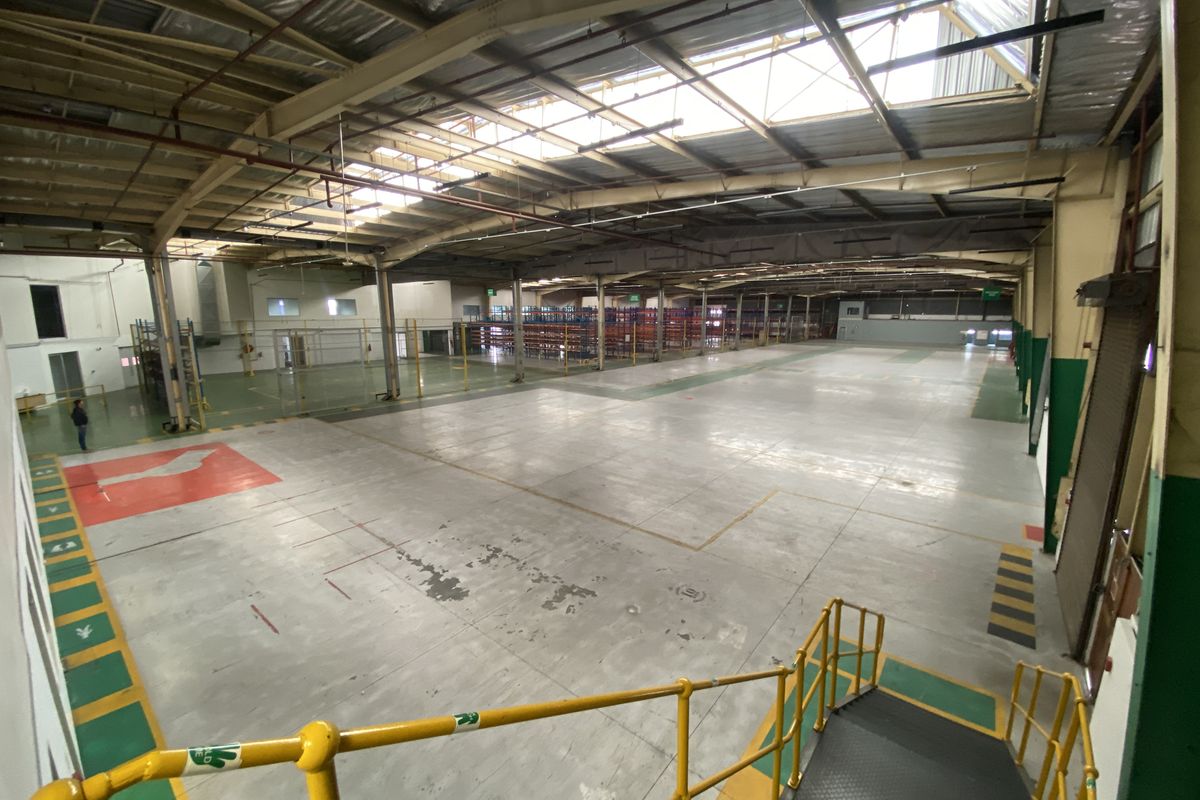 Expansive industrial warehouse space featuring high ceilings with skylights, durable concrete flooring, and integrated metal staircase access.