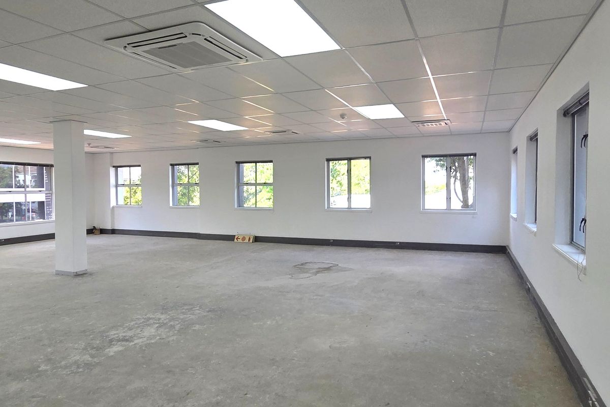 A spacious, open-plan office area featuring a suspended ceiling, recessed lighting, integrated cassette air conditioning, and large windows providing ample natural light.