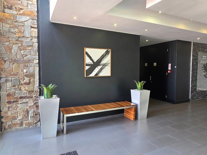 Modern office entrance lobby featuring a striking stone-clad feature wall, dark accent wall, recessed ceiling lighting, and contemporary tiled flooring.