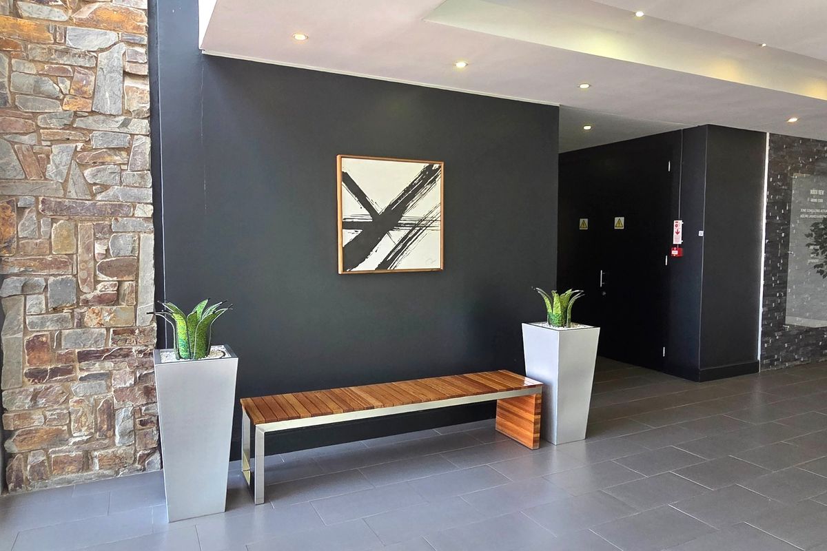 Modern office entrance lobby featuring a striking stone-clad feature wall, dark accent wall, recessed ceiling lighting, and contemporary tiled flooring.