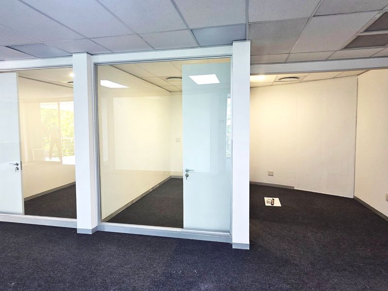 Modern office space featuring glass partition walls, suspended ceilings with recessed lighting, and clean carpet flooring, offering a professional and bright work environment.