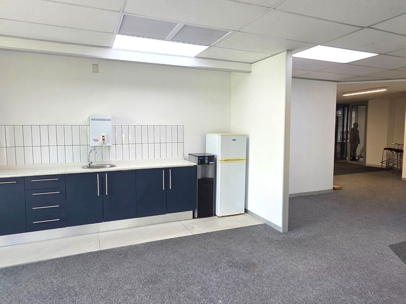 A functional office kitchenette featuring dark blue cabinetry, a stainless steel sink, tiled backsplash, and a drop ceiling with integrated lighting.